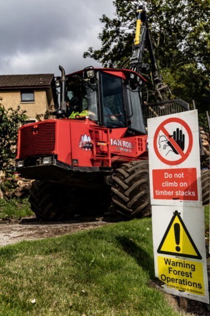 Timber harvesting machine alongside public warning signs
