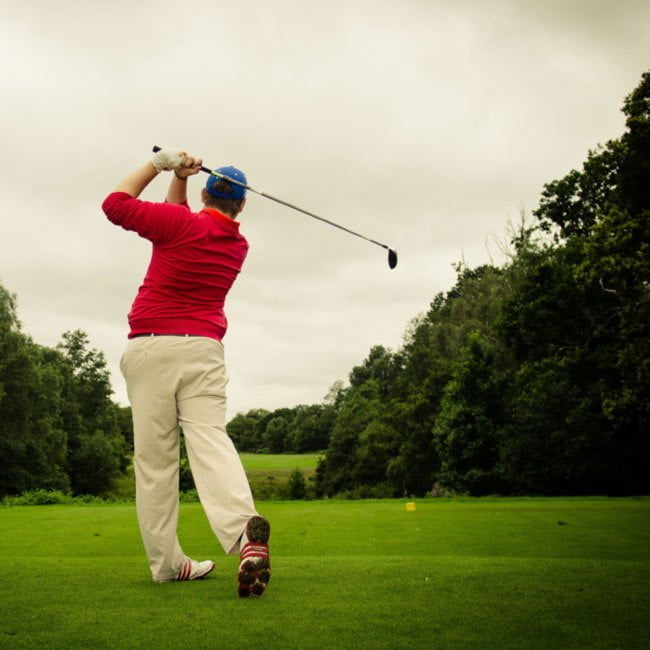 Male golfer hitting tee shot down a wooded fairway
